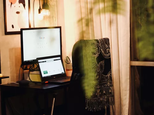 a desk with computer screens and a chair with a shawl represent a home office