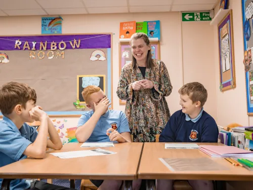 a female tutor smiles as she gives a class to three boys