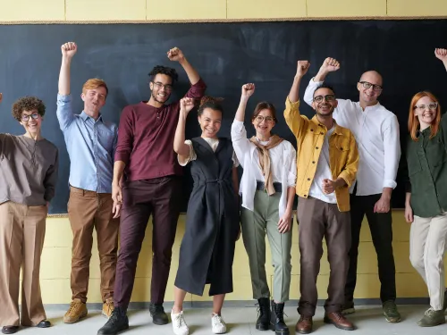 four men and two women raise a celebratory hand in front of a chalkboard