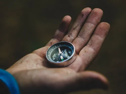 a child's muddy hand holding a small metal compass