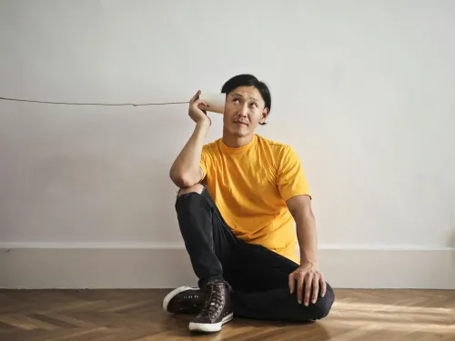 a man in a yellow t-shirt listens to a cup attached to some string